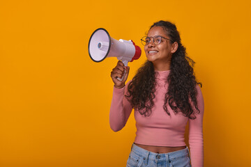 Young attractive Indian woman student in glasses and casual wear holding megaphone inviting campus...