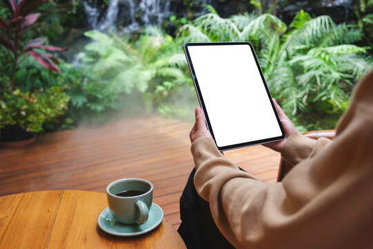 Mockup image of a woman holding digital tablet with blank white desktop screen while drinking coffee in the garden