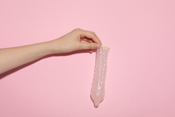 An unfolded condom in a hand on a pink background