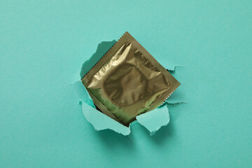 Condom on the background of torn turquoise paper
