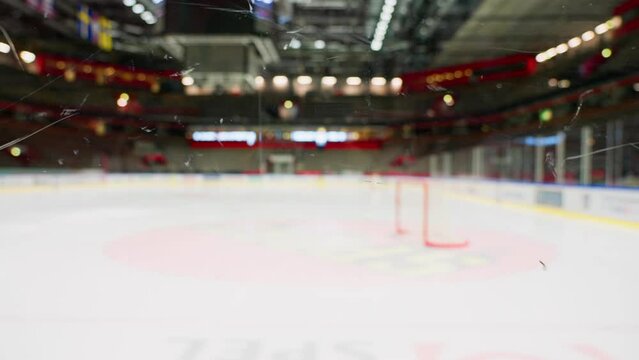 Out of focus hockey arena with in focus plexiglass in foreground. Dolly left.
