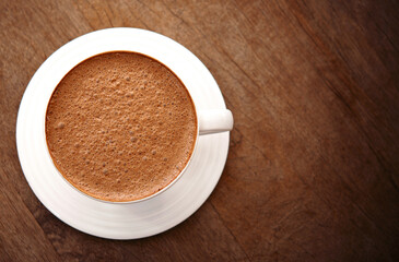 Hot chocolate in white ceramic mug on wooden table.
