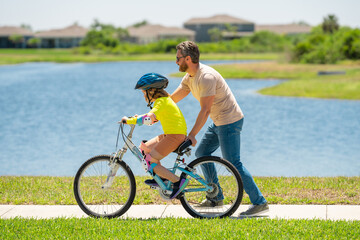 Father and son learning to ride a bicycle having fun together at Fathers day. Father teaching his son cycling on bike in american neighborhood. Father and son concept. Father support son.