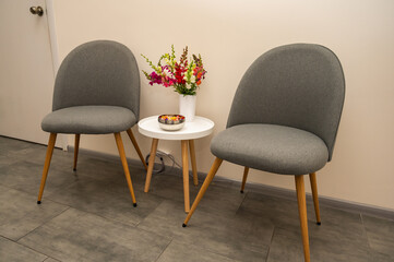 two soft armchairs in a light room, an office near a round table, for waiting, on which there are fresh flowers in a vase, next to a light wall in the interior of a hotel