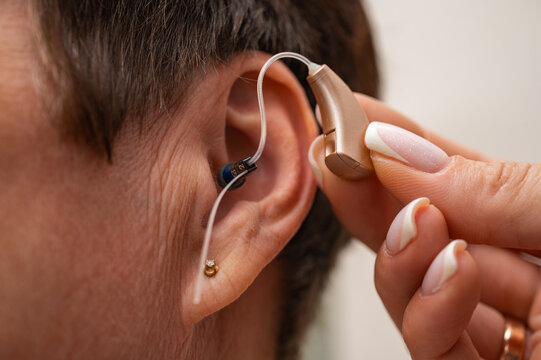 A woman tries on a hearing aid hidden in her ear on a light background. Restoration of hearing. Technical means