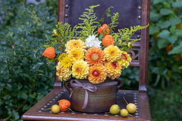 rustikaler Blumenstrauß mit gelben und orange Dahlien, Physalis und Goldrute im Terracotta-Topf