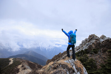 Woman hiker enjoy the view on mountain top cliff edge face the snow capped mountains in tibet