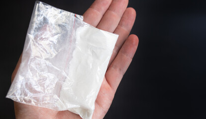 Mans hand holding in hand plastic packet with cocaine powder or another drugs. Drug dealer proposes...