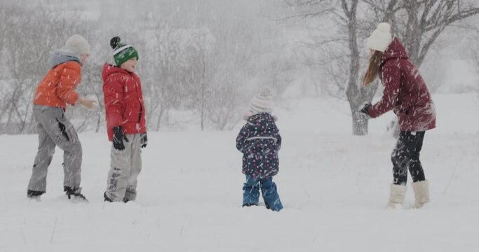 Children have fun outdoors during snowfall. Big family or friends playing at snowballs in winter park. Heavy snowfall