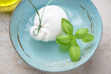 Turquoise bowl with burrata cheese in brine and green basil, horizontal shot, middle close-up, selective focus