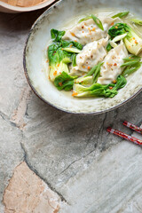 Bowl with asian dumplings and pok choy in broth, vertical shot on a grey granite background with copy space, selective focus