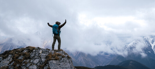 Woman hiker enjoy the view on mountain top cliff edge face the snow capped mountains in tibet