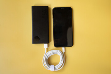 Power Bank charges your smartphone on a yellow background. Universal external battery for gadgets free space. 