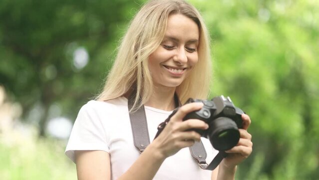 Portrait of pretty young blond woman photographer hold digital camera and looking at photos on screen at green park Charming young tourist female taking pictures during vacation outdoors