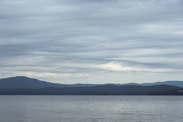 Dense gray thunderstorm cumulus clouds and a lake, water with waves. A gloomy rainy day at sea with beautiful clouds