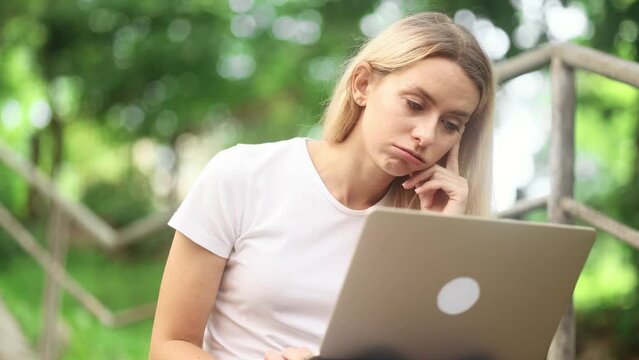 Tired exhausted boring young blond woman freelancer with laptop dozing sitting on grass at park Portrait of overworked self employee worker absolutely unmotivated next to computer outdoors
