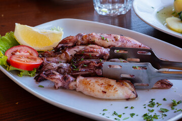 A dish of sea squid on a plate with lemon and tomatoes