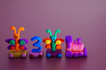 Toy train made of plasticine with butterflies and the number 3. Birthday. A festive event. Color background.