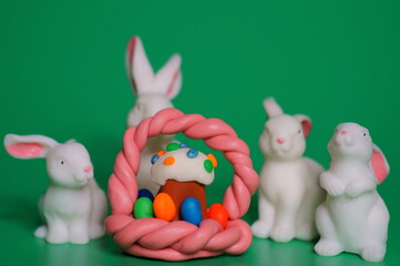 Toy white rabbits on a green background. Next to the basket with an Easter cake.