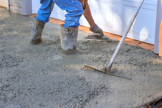 Concrete leveling workers on construction site with mix trowel leveling to concrete driveway