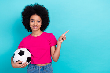 Photo of good mood adorable girl wear pink t-shirt holding soccer ball indicating at sale empty space isolated on blue color background