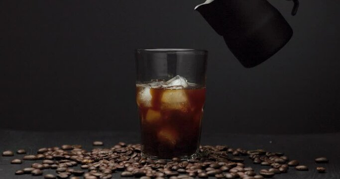 Milk cream is poured into an iced coffee. Coffee cold drink with ice and milk.
