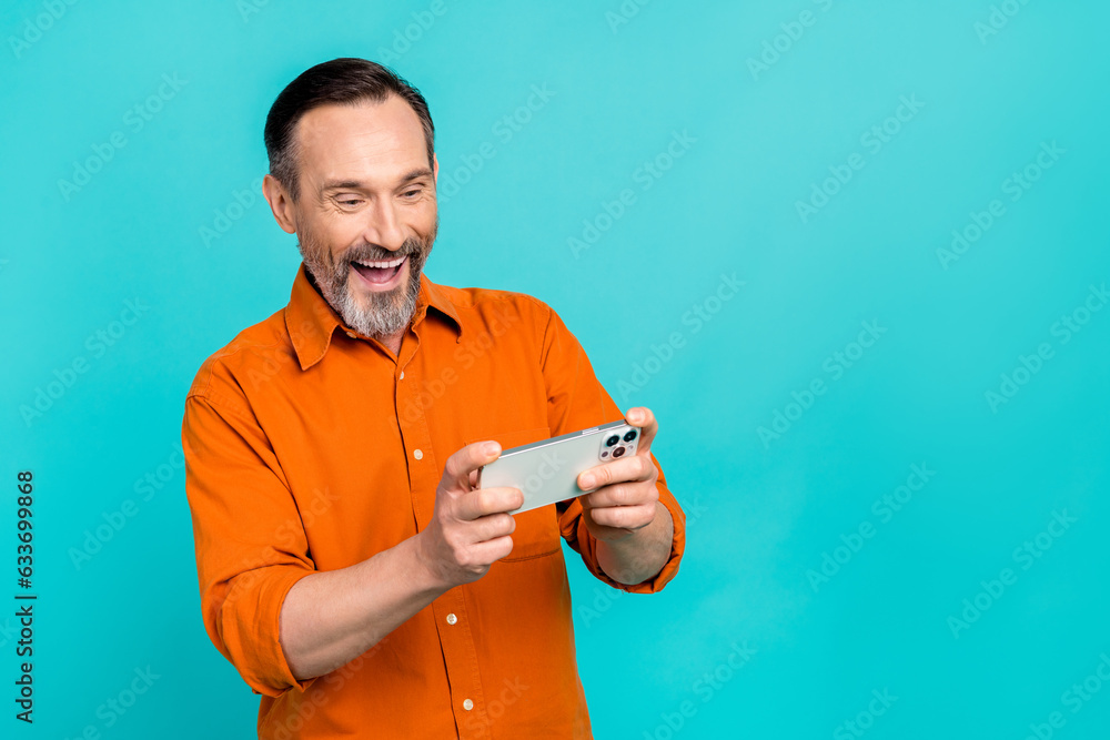 Sticker Portrait of funky pensioner man addicted play video games hold smartphone enjoy spend his lunch free time isolated on blue color background