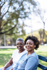 Smiling adult woman and her older mother sitting on a park bench