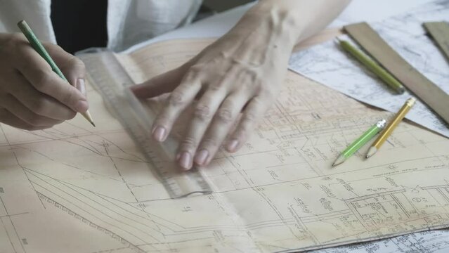 Engineer draws the project using ruler and a pencil. Papers and drawings on the desk. Architect works with blueprints. Close-up of female hands drawing lines on the old large format paper 