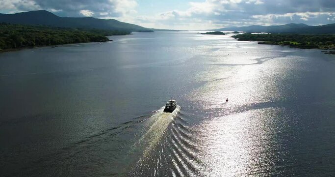 A 4K rising following aerial shot of a tourist boat sailing  towards the open sea in the sunshine in Kenmare Bay