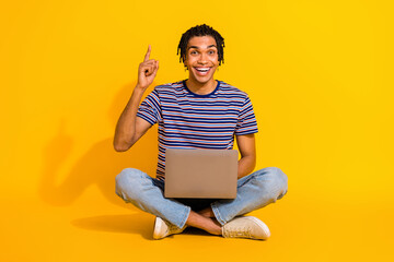 Full length portrait of overjoyed handsome guy sit floor use netbook point finger up empty space isolated on yellow color background