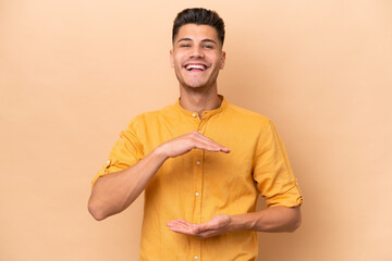 Young caucasian man isolated on beige background holding copyspace imaginary on the palm to insert...