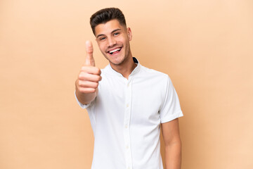 Young caucasian man isolated on beige background with thumbs up because something good has happened