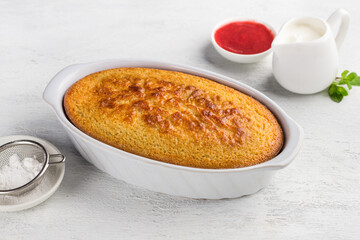 Freshly prepared mannik, semolina pie in the form with sour cream and berry sauce on a light gray background