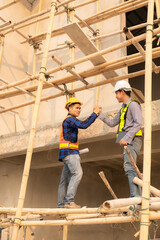 Fototapeta premium Two Asian male engineers shaking hands and working together Hope stands on the architectural construction site on the structure industry. Wear a helmet with a checkered shirt.