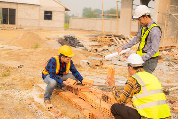 Architects and engineers working together sketching building plans and discussing at construction site wearing uniforms and helmets standing on construction site about large industrial architecture.