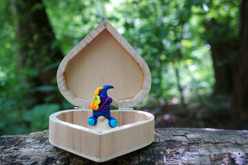 A fairy-tale dwarf made of plasticine and a wooden box in the form of a heart. A fictional character. A vivid image.