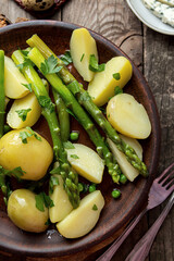 Boiled potato with grilled green asparagus on brown plate over on old wooden background. Overhead. Rustic style.