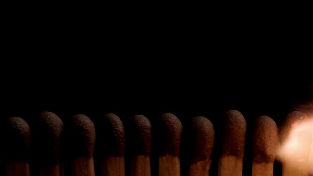 In a captivating slow-motion video, a line of matchsticks are ignited in sequence from right to left. The close-up showcases each individual flame as it spreads, creating a synchronized dance of fire