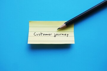 Pencil wrote on blue background stick note CUSTOMER JOURNEY - marketing buzzword, actions customers...
