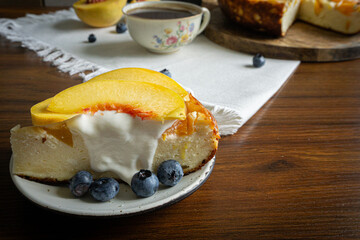 A piece of cheesecake with sour cream and peaches on the top. Coffee in vintage porcelain cup on the background