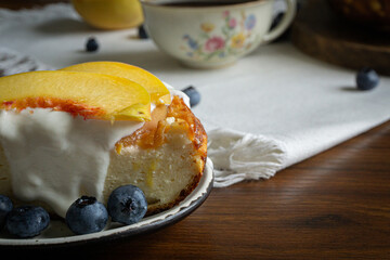 A piece of cheesecake with sour cream and peaches on the top. Coffee in vintage porcelain cup on the background