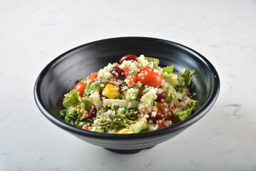 couscous healthy grain salad bowl with corn, bean, carrot and salad dressing sauce on white marble...