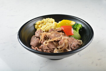stir fried bbq bulgogi beef rice bowl with scrambled eggs and fried vegetable salad in black bowl on white marble table background chef cook healthy poke protein bowl halal vegan food menu