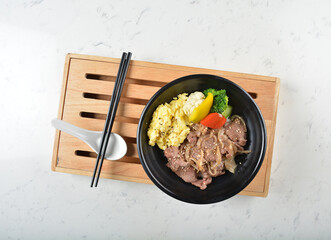 stir fried bbq bulgogi beef rice bowl with scrambled eggs and fried vegetable salad in black bowl on white marble table background chef cook healthy poke protein bowl halal vegan food menu