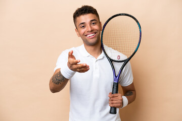 Young brazilian handsome man playing tennis isolated on beige background shaking hands for closing...