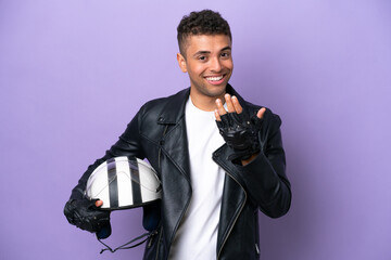 Young Brazilian man with a motorcycle helmet isolated on purple background inviting to come with hand. Happy that you came