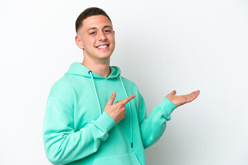 Young brazilian man isolated on white background holding copyspace imaginary on the palm to insert...