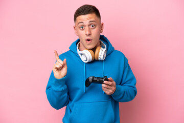 Young brazilian man playing with a video game controller isolated on pink background intending to realizes the solution while lifting a finger up