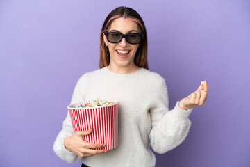 Young caucasian woman isolated on blue background with 3d glasses and holding a big bucket of popcorns
